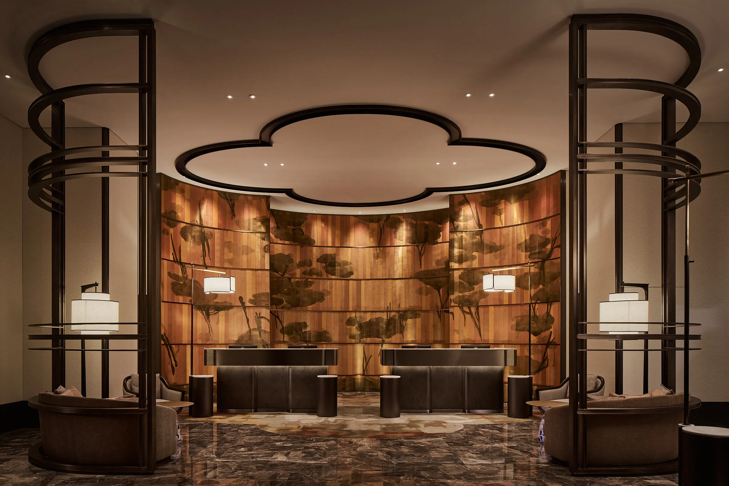 Warmly lit hotel lobby with sculptural dark wood details and a golden mural behind the reception desk.